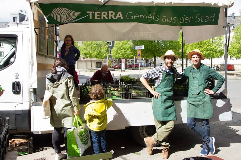 A group of farmers celebrating at a local market stand with fresh produce on display.