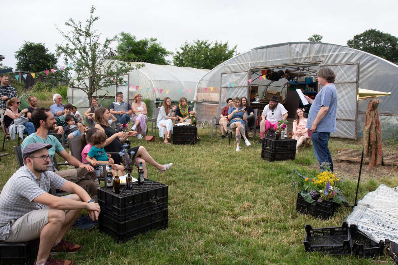People gathered outside a greenhouse, engaged in conversation and handling plants