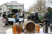 Bottles of apple cider displayed on a table with a wooden barrel at a market